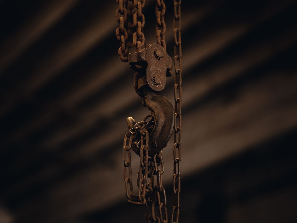 A worn steel chain and hook hanging in a dark shop.